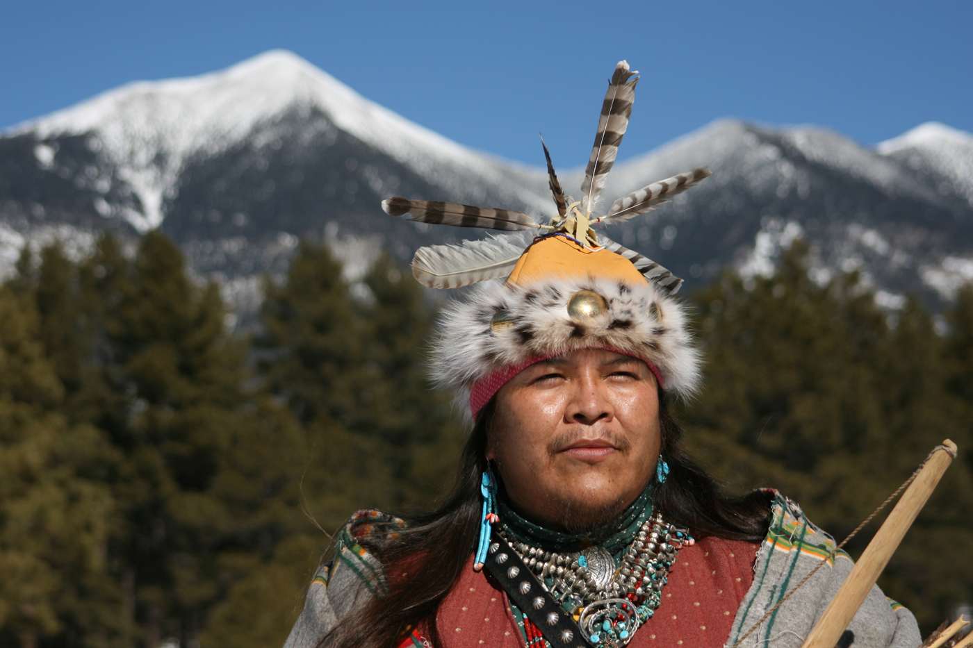 A Native American man in traditional regalia before the snow-capped San Francisco Peaks near Flagstaff, Arizona