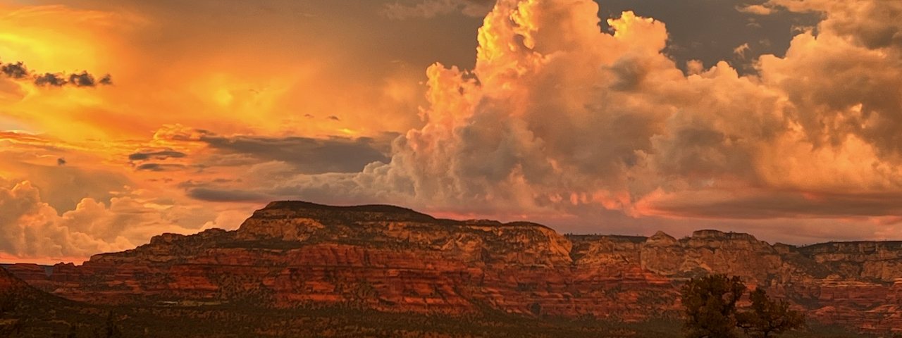 Monsoon thunderclouds glowing orange at sunset above a red rock mesa in Northern Arizona