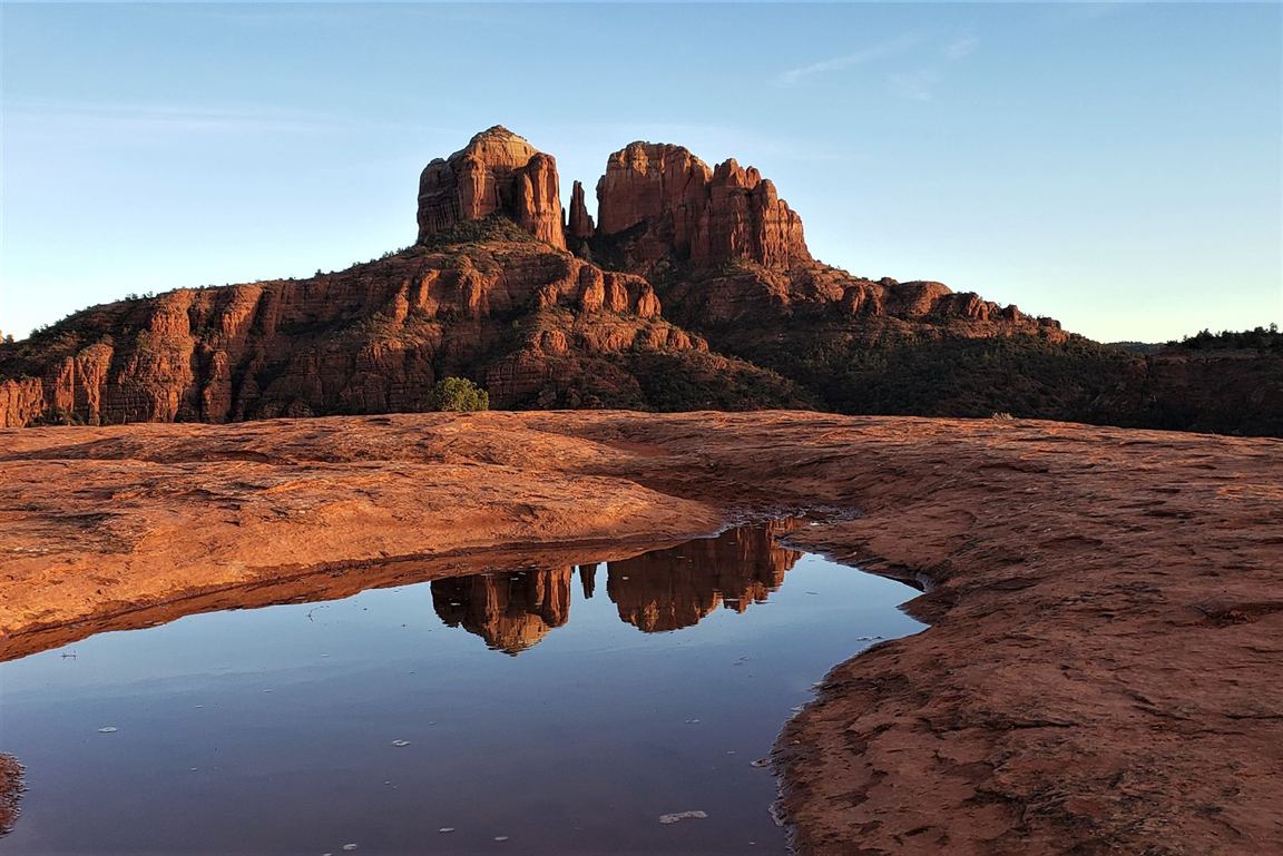 Cathedral Rock in Sedona reflected in a slickrock puddle under a clear blue sky at golden hour