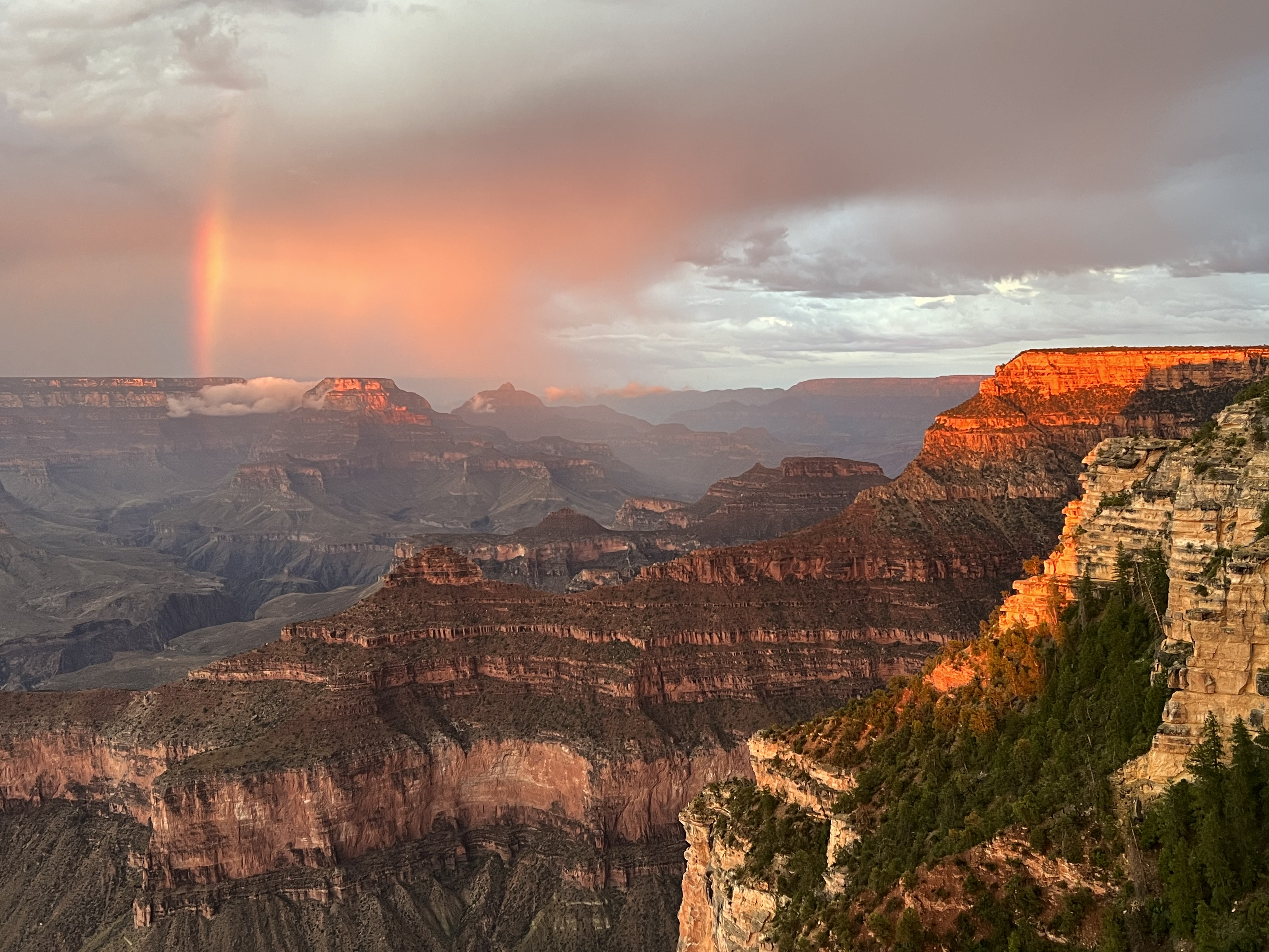 Warm storm light and a rainbow over the Grand Canyon at sunset