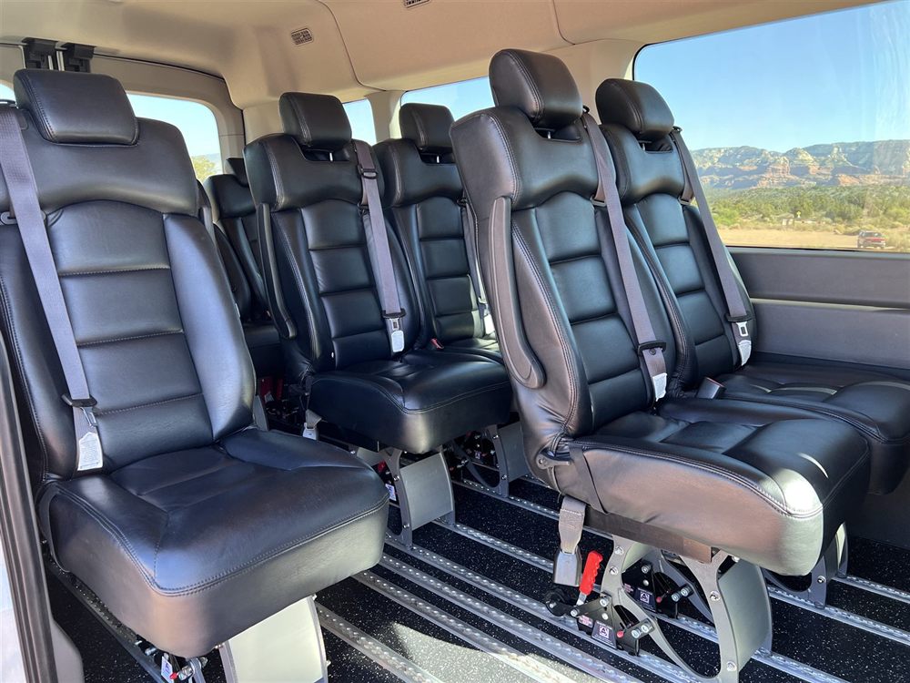 Rows of leather captain's chairs inside the 2023 Ford Transit, with Sedona red rock views through the window