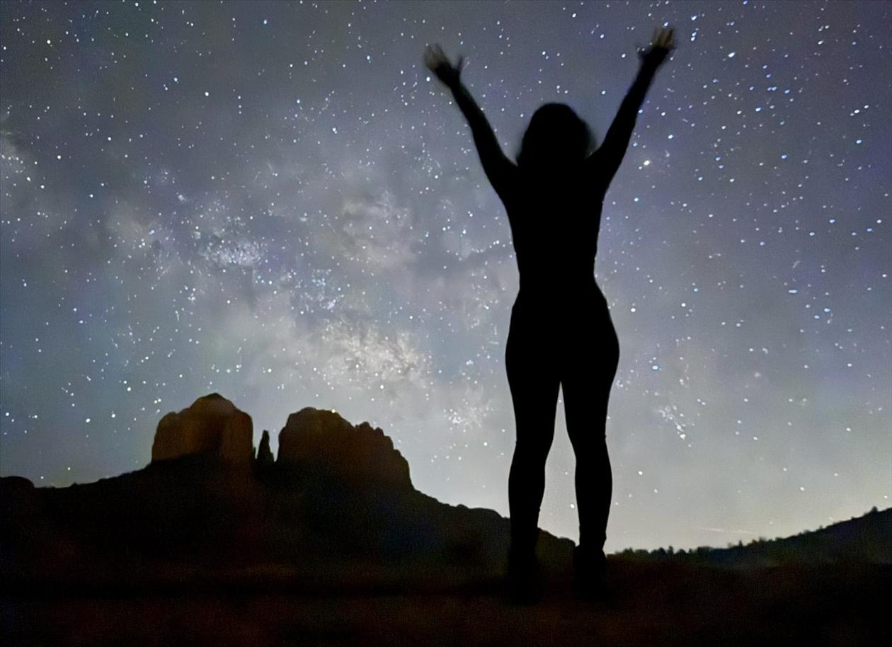 A guest raises their arms under the Milky Way near Cathedral Rock at night